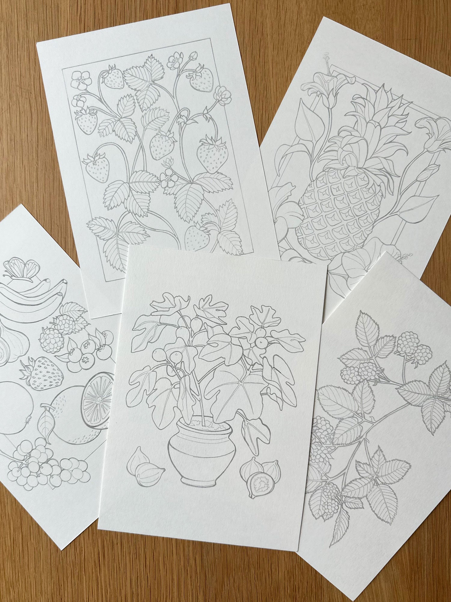 Set of coloring pages with floral and fruit designs on a wooden surface